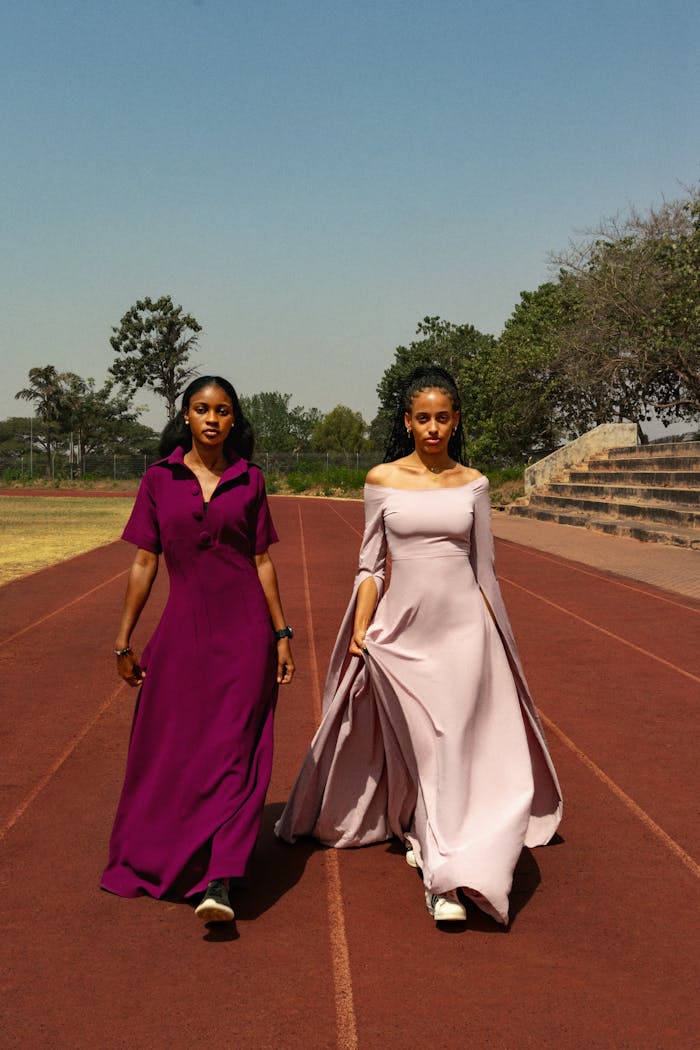 Services Two women elegantly dressed walking on an outdoor track amidst nature, showcasing fashion in motion.
